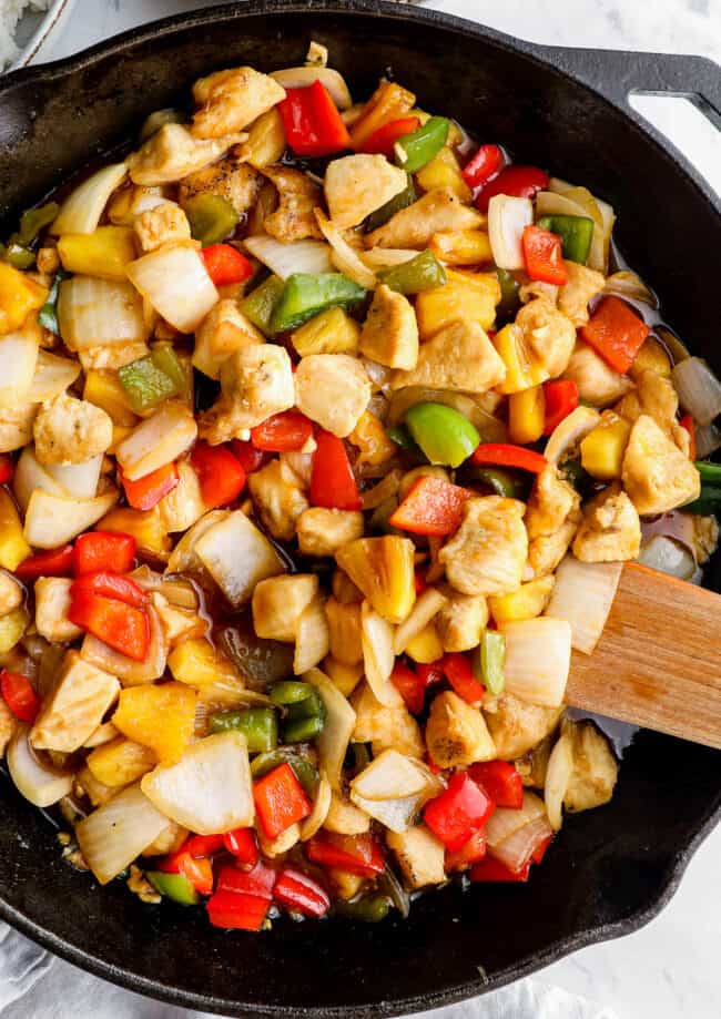 sweet and sour chicken in skillet with wooden spoon