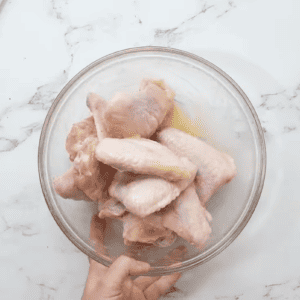 A person is holding chicken wings in a bowl.