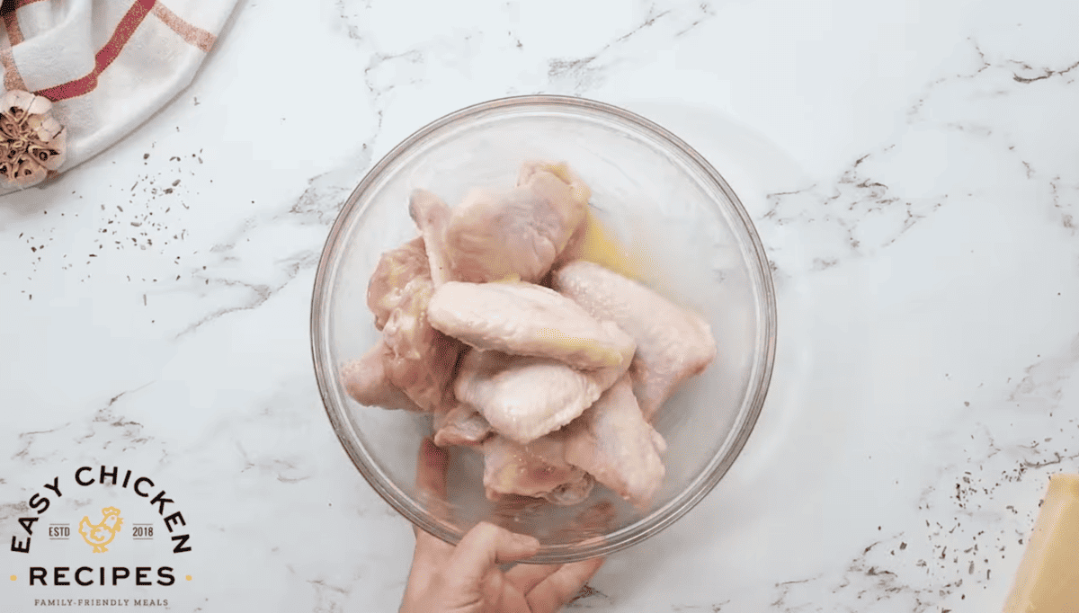 A person is holding chicken wings in a bowl.