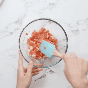 mixing diced tomatoes and onions in a glass bowl.