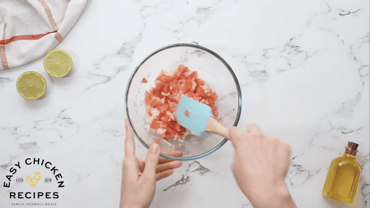 mixing diced tomatoes and onions in a glass bowl.