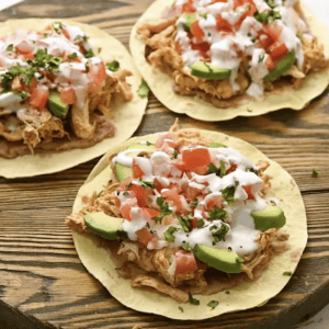 chicken tostadas topped with sour cream and cilantro on a round wooden cutting board.