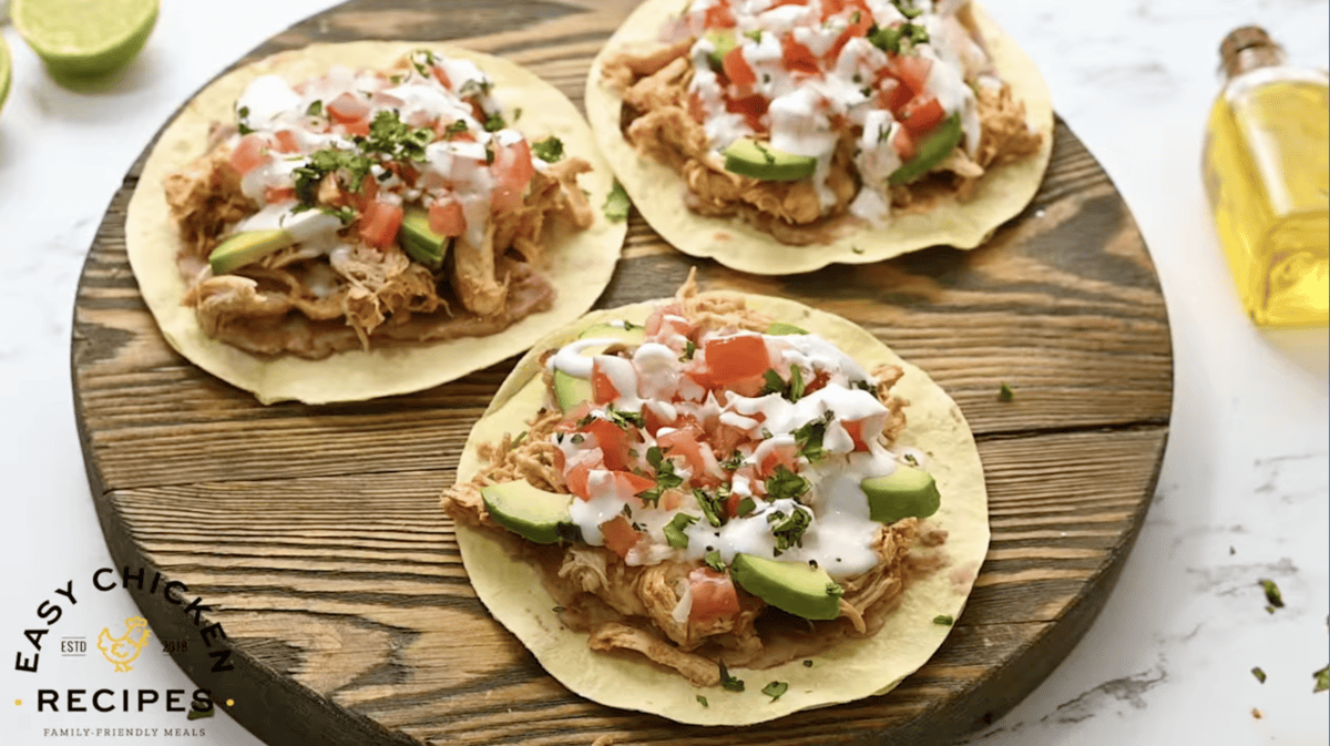 chicken tostadas topped with sour cream and cilantro on a round wooden cutting board.
