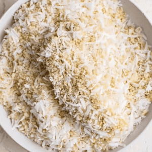 a coconut breaded raw chicken tender in a bowl of breadcrumbs.