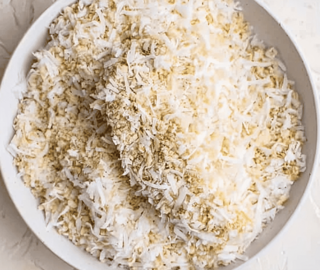 a coconut breaded raw chicken tender in a bowl of breadcrumbs.