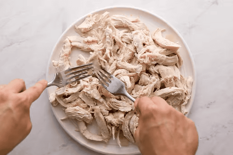 Two forks shredding chicken breasts.
