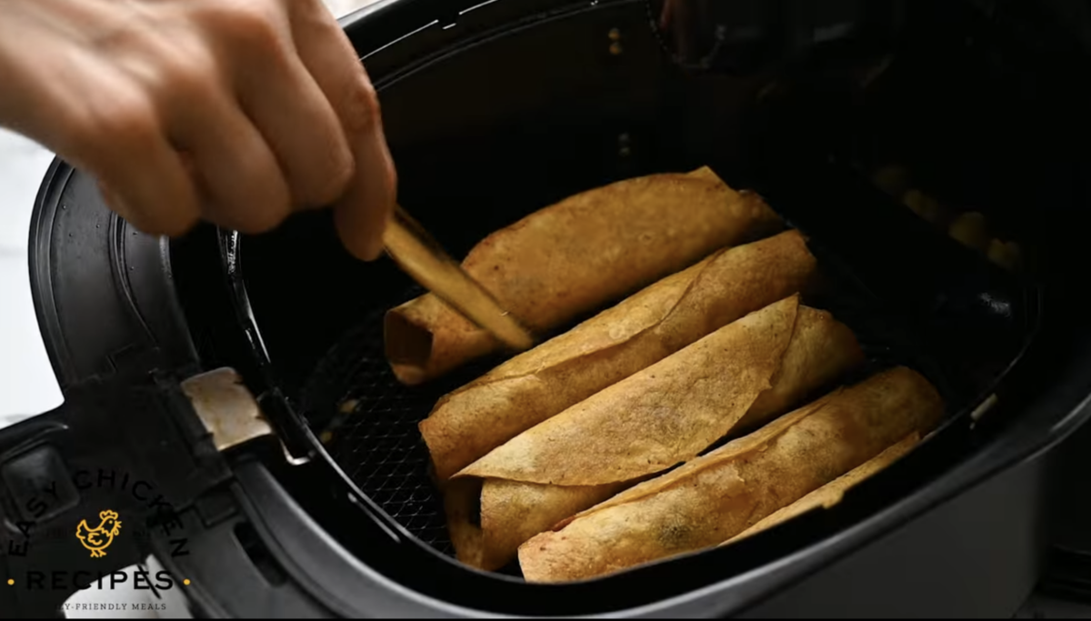 A person is putting taquitos into an air fryer.