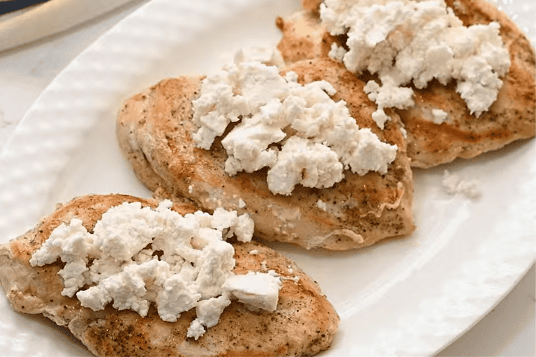 Cooked chicken breasts on a plate, topped with goats cheese to make Cabbarra's chicken bryan copycat recipe.