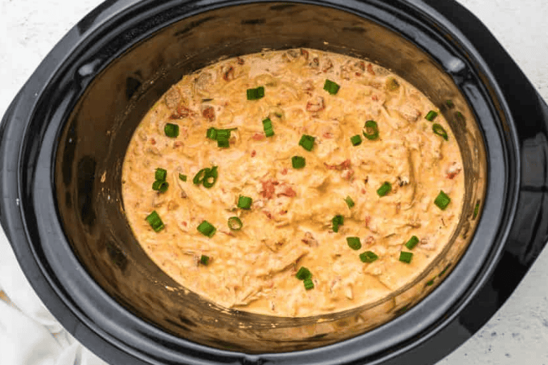 Crockpot queso chicken topped with green onions in a slow cooker.