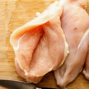Three chicken breasts on a chopping board, with one sliced open.