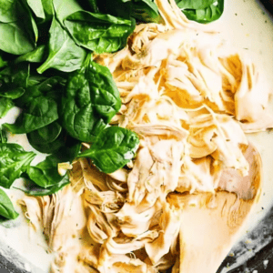 shredded chicken and spinach folded into creamy sauce with a wooden spoon.