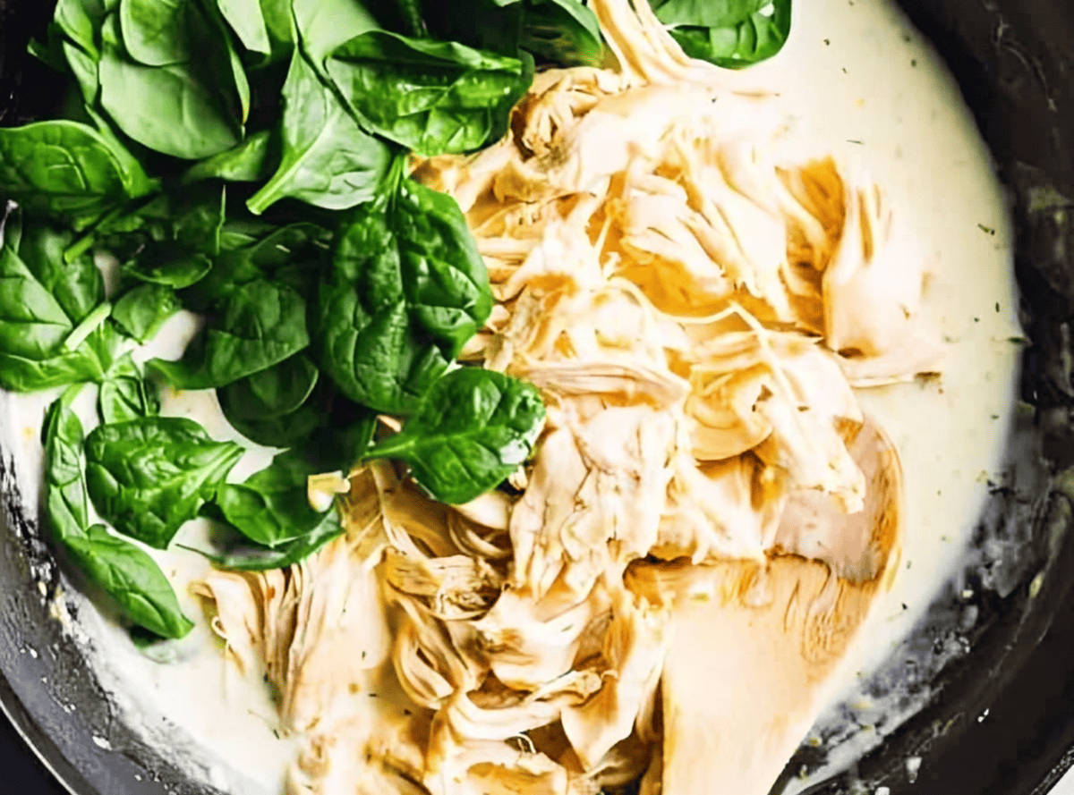 shredded chicken and spinach folded into creamy sauce with a wooden spoon.