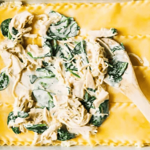 spreading chicken spinach filling over lasagna noodles with a wooden spoon.