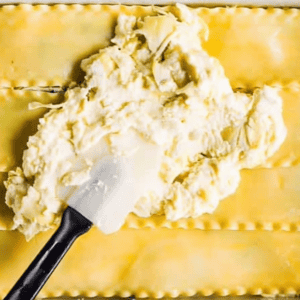 spreading cheesy artichokes over lasagna noodles with a rubber spatula.