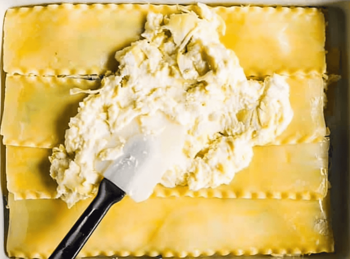 spreading cheesy artichokes over lasagna noodles with a rubber spatula.