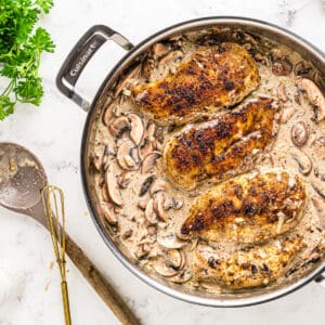 smothered chicken breasts and mushroom sauce in a pan.