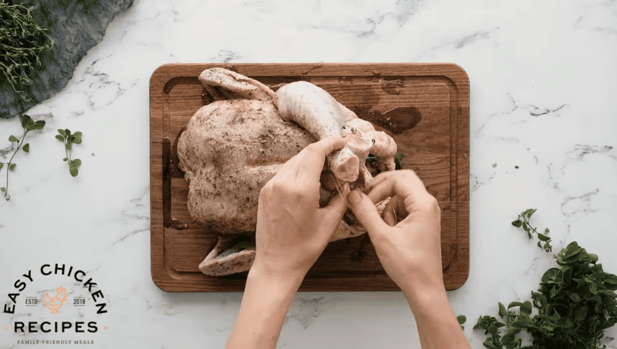 The legs of the raw chicken are being tied with twine. 