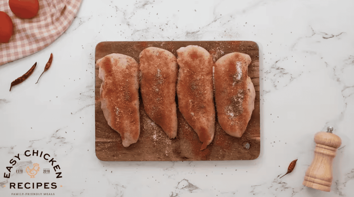 Four chicken breasts are seasoned on a cutting board.