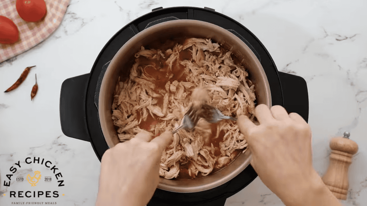 Chicken is being shredded in a pressure cooker. 
