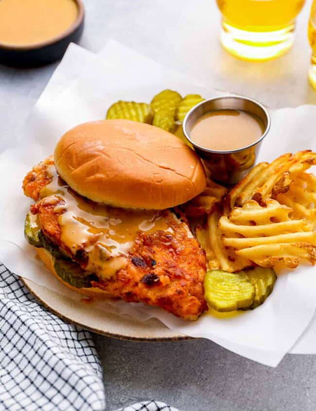 three-quarters view of a copycat chick fil a sandwich on a white plate with pickle slices, waffle fries, and chick fil a sauce.