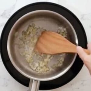 sautéeing garlic, onion, and ginger in a saucepan with a wooden spatula.