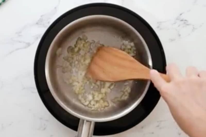 sautéeing garlic, onion, and ginger in a saucepan with a wooden spatula.