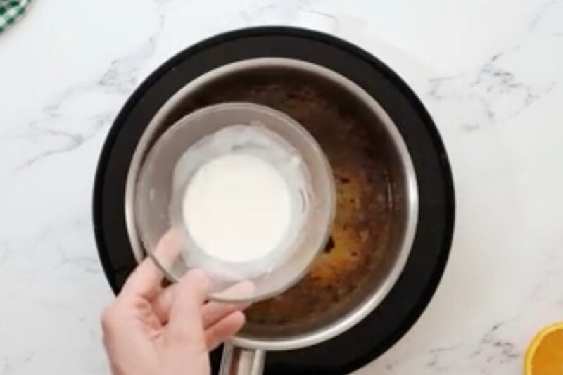 adding a cornstarch slurry to orange sauce.