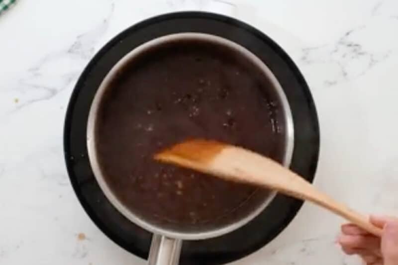 thickened orange sauce in a saucepan with a wooden spatula.