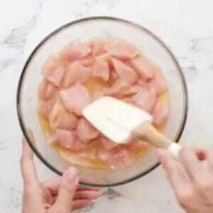 stirring chicken pieces in raw egg in a bowl with a rubber spatula.