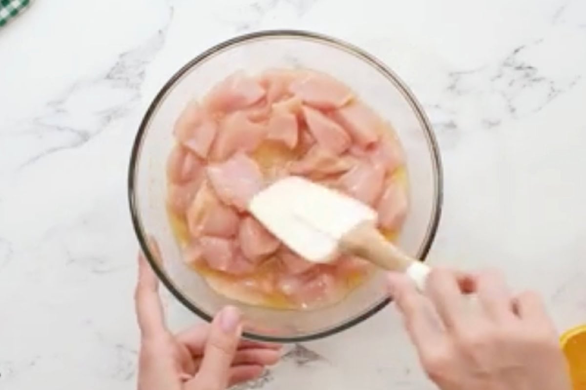 stirring chicken pieces in raw egg in a bowl with a rubber spatula.