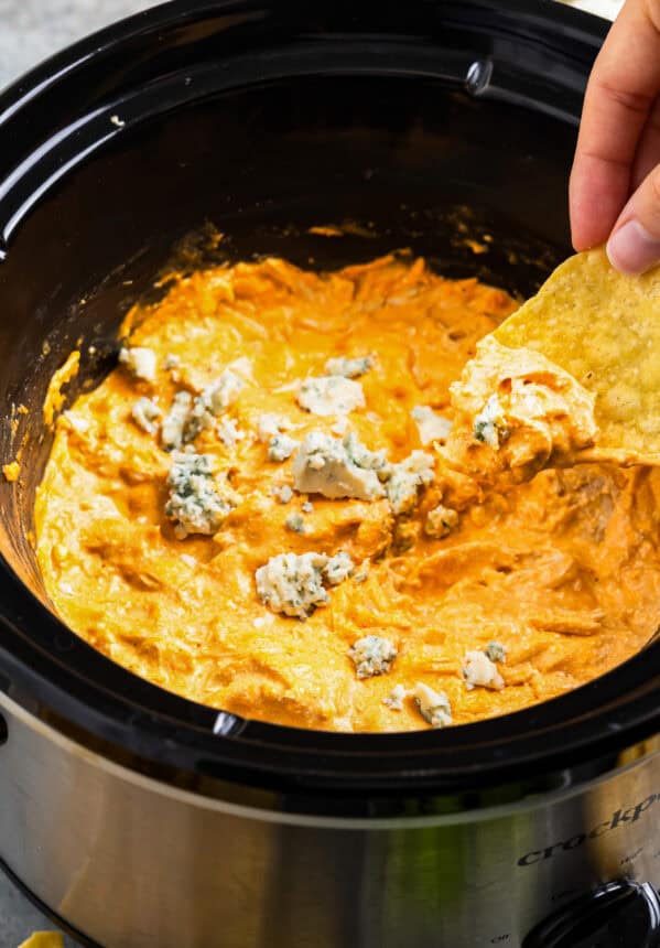 dipping a tortilla chip into buffalo chicken dip in a crockpot.