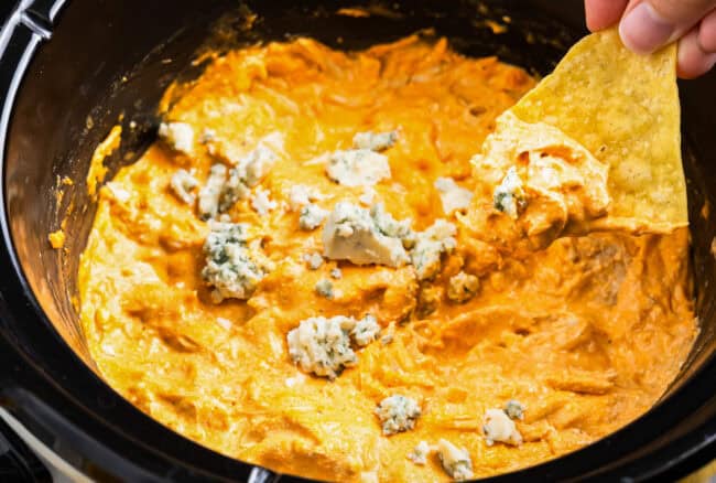 dipping a tortilla chip into buffalo chicken dip in a crockpot.