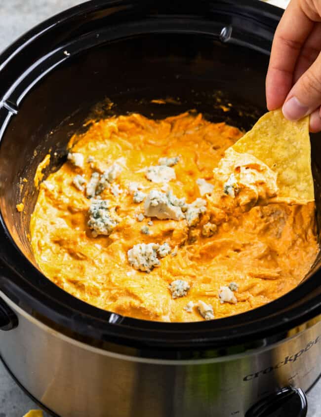 dipping a tortilla chip into buffalo chicken dip in a crockpot.