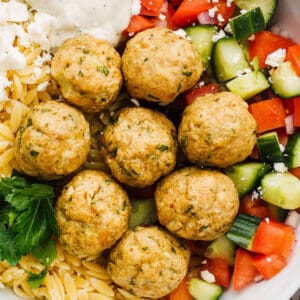 up close Greek chicken meatballs over veggies, rice and tzatziki sauce.