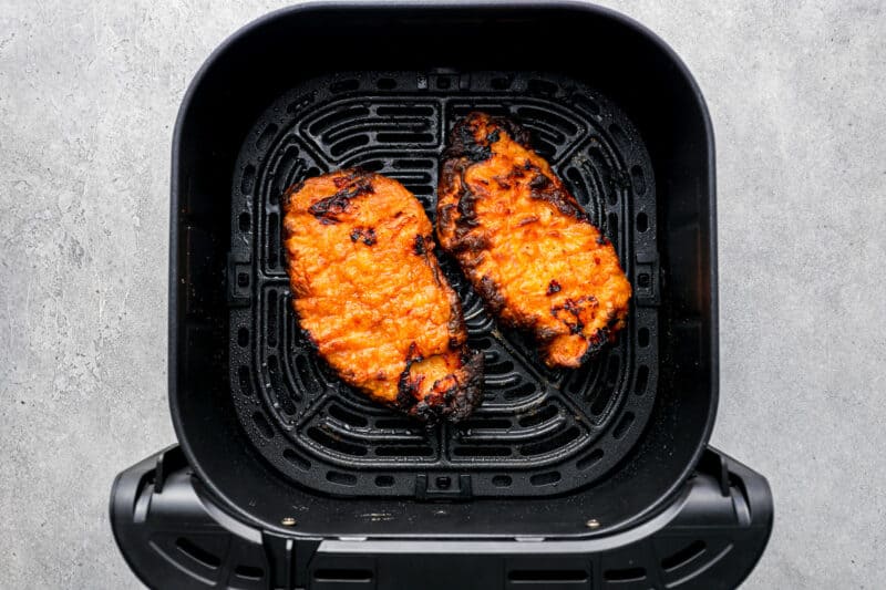 2 cooked breaded chicken breasts in the basket of an air fryer.