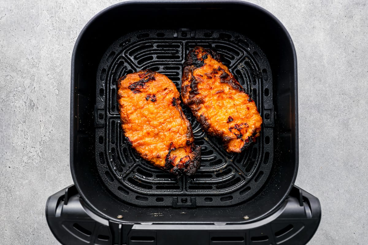 2 cooked breaded chicken breasts in the basket of an air fryer.