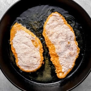 chicken frying in a cast iron pan.