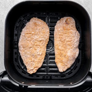 2 raw breaded chicken breasts in the basket of an air fryer.
