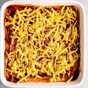 bbq chicken dip topped with bbq sauce and cheese in a baking dish.