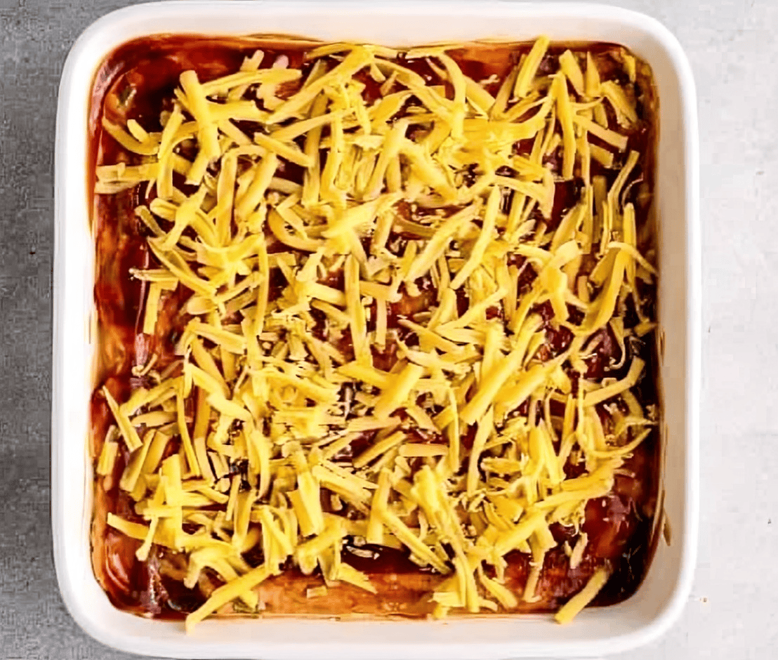 bbq chicken dip topped with bbq sauce and cheese in a baking dish.