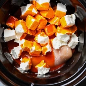 buffalo sauce drizzled over cubed cream cheese and raw chicken in a crockpot.