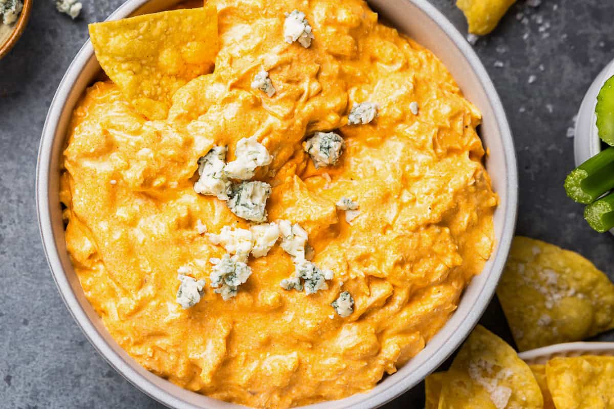 overhead view of crockpot buffalo chicken dip in a white bowl with blue cheese and tortilla chips.