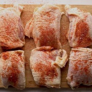 Seasoned chicken thighs on a wooden chopping board