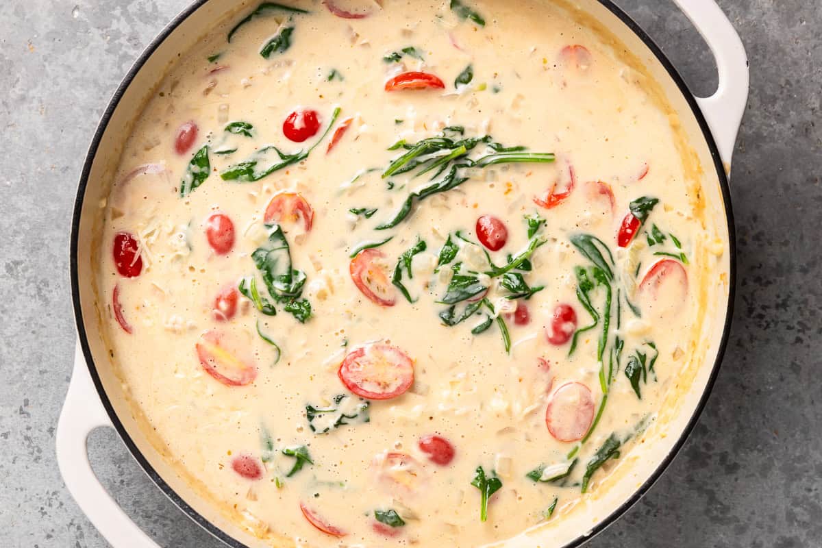 cream sauce with spinach and tomatoes in a skillet.