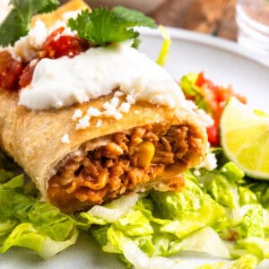 side view of a cut chicken chimichanga on a white plate with lettuce.
