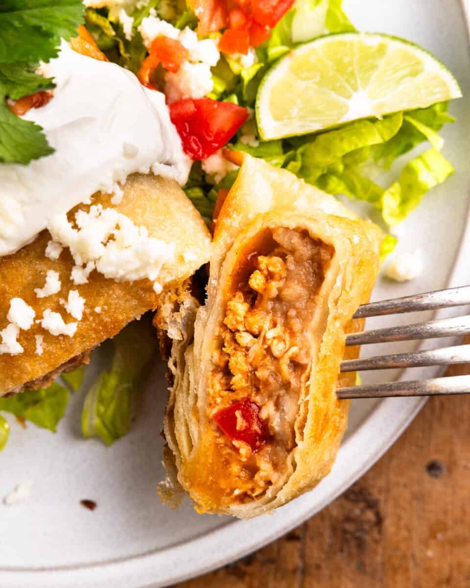 a fork holding a cut chicken chimichanga upright to show the filling.