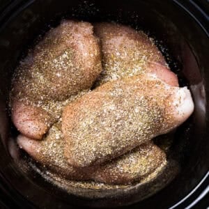 seasoned raw chicken breasts in a crockpot.