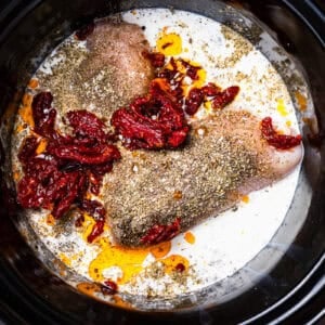 seasoned chicken breasts, cream, and sun-dried tomatoes in a crockpot.