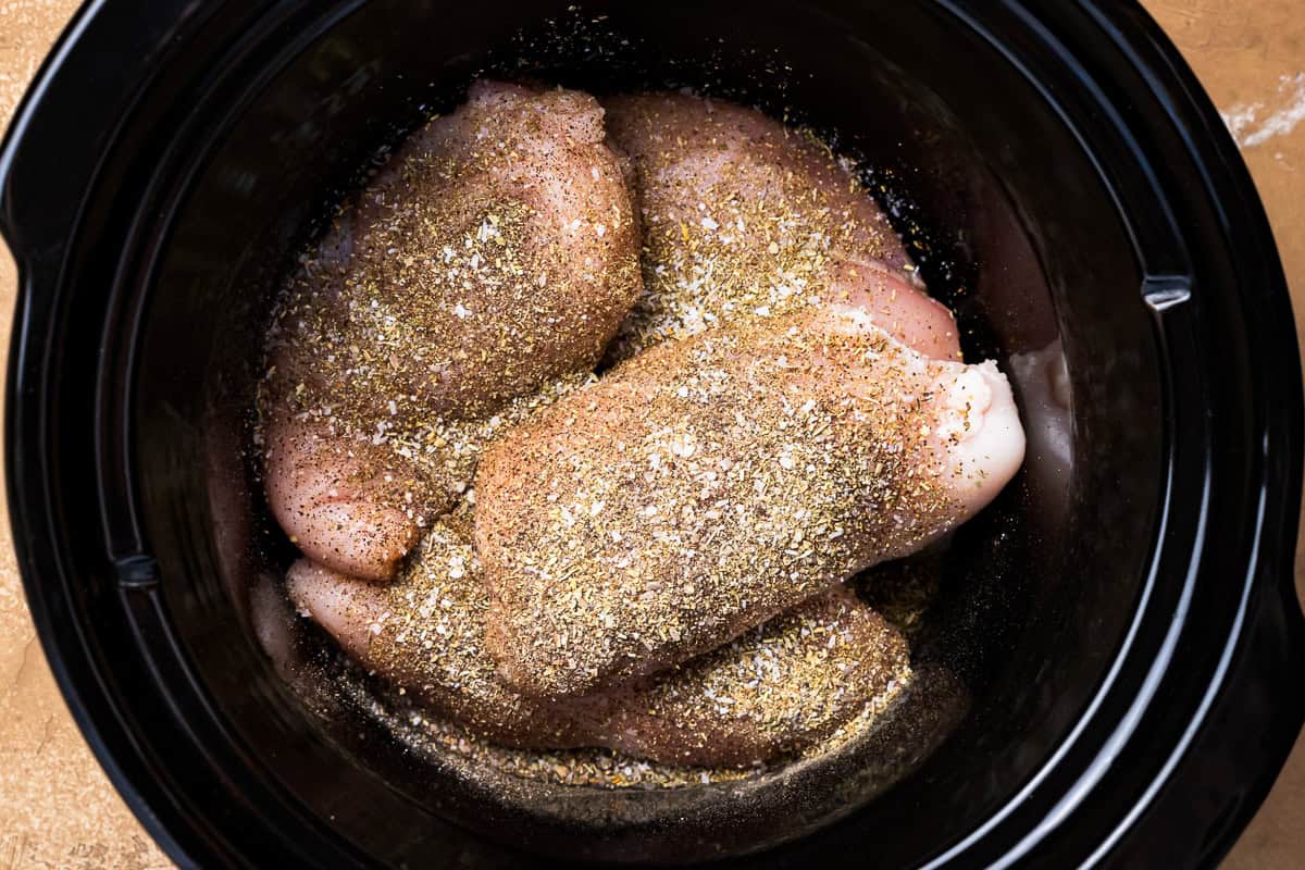 seasoned raw chicken breasts in a crockpot.