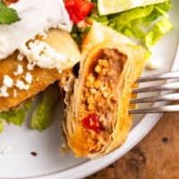 a fork holding a cut chicken chimichanga upright to show the filling.
